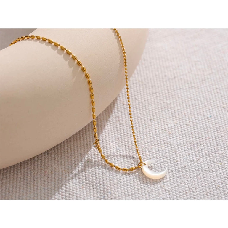 A stylish woman wearing a beautiful 18K gold plated moon pendant necklace. The natural shell pendant shines against her skin, adding a touch of celestial charm to her outfit. The delicate yet sturdy chain ensures the pendant sits beautifully on her neckline. The necklace is waterproof, making it perfect for daily wear