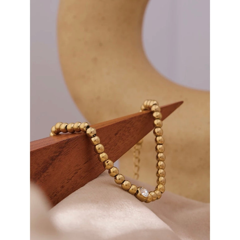 A close-up of a woman's wrist, featuring a minimalist gold bead bracelet adding a touch of luxury and style to her outfit
